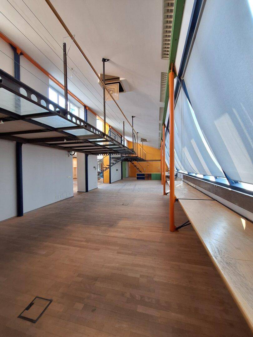 Weitläufiger Innenraum mit Holzboden, großen Fenstern und einer modernen, offenen Gestaltung.