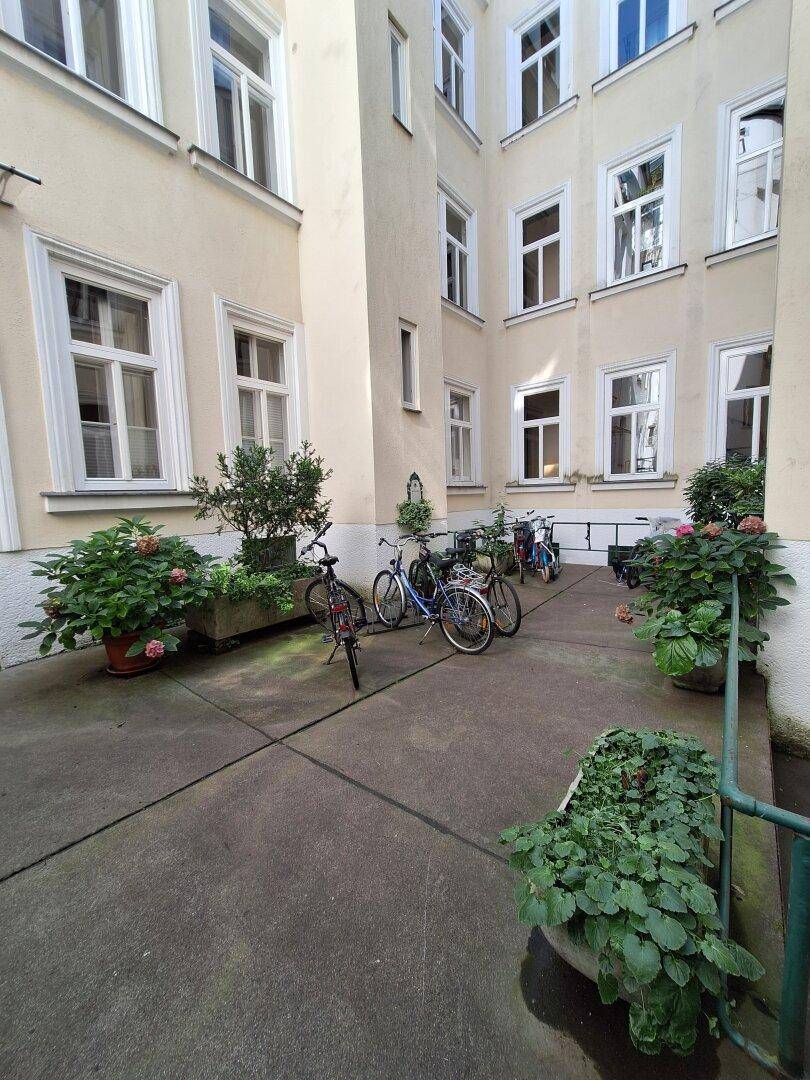 Ruhiger Innenhof mit Fahrrädern, Topfpflanzen und der Fassade eines Mehrfamilienhauses.