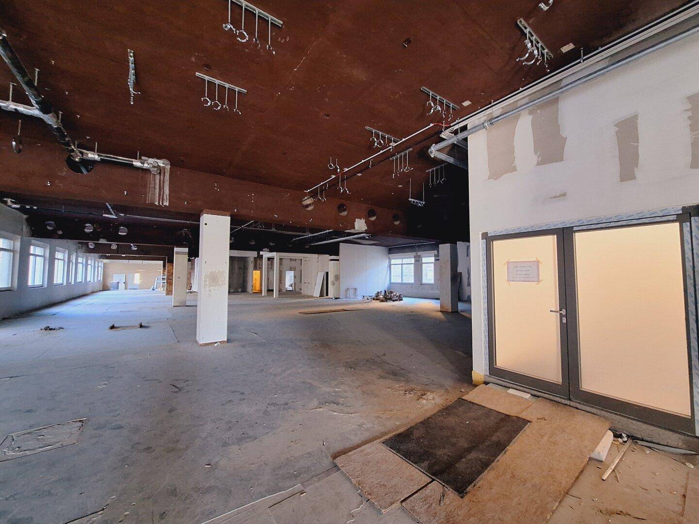 Geräumiger Gewerberaum im Rohbau mit großen Türen und sichtbaren Deckeninstallationen.