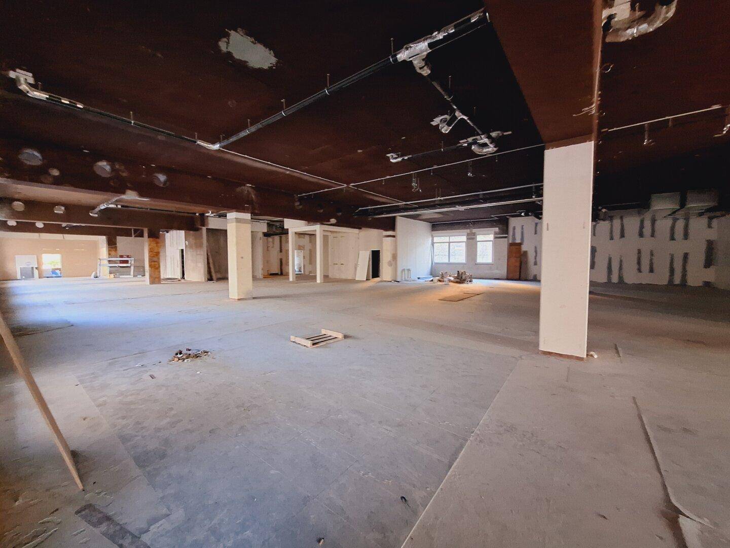 Großer, offener Gewerberaum im Rohbau mit sichtbaren Installationen und hohen Decken.