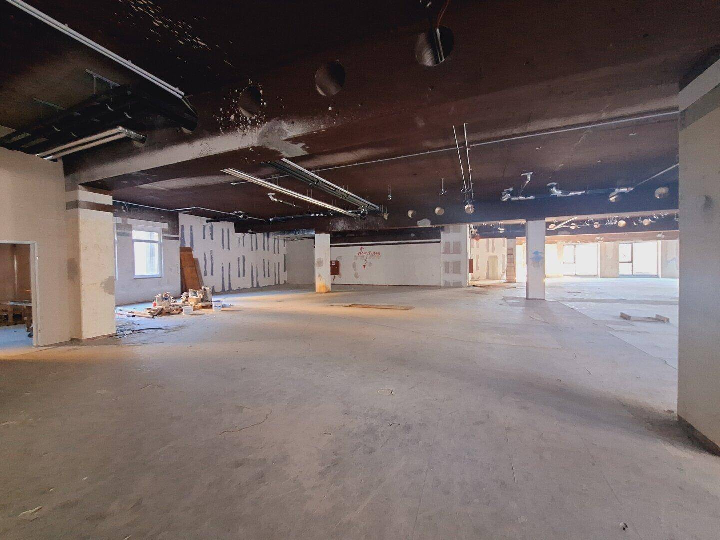 Weitläufiger Gewerberaum im Rohbau mit sichtbaren Deckeninstallationen und viel Tageslicht.