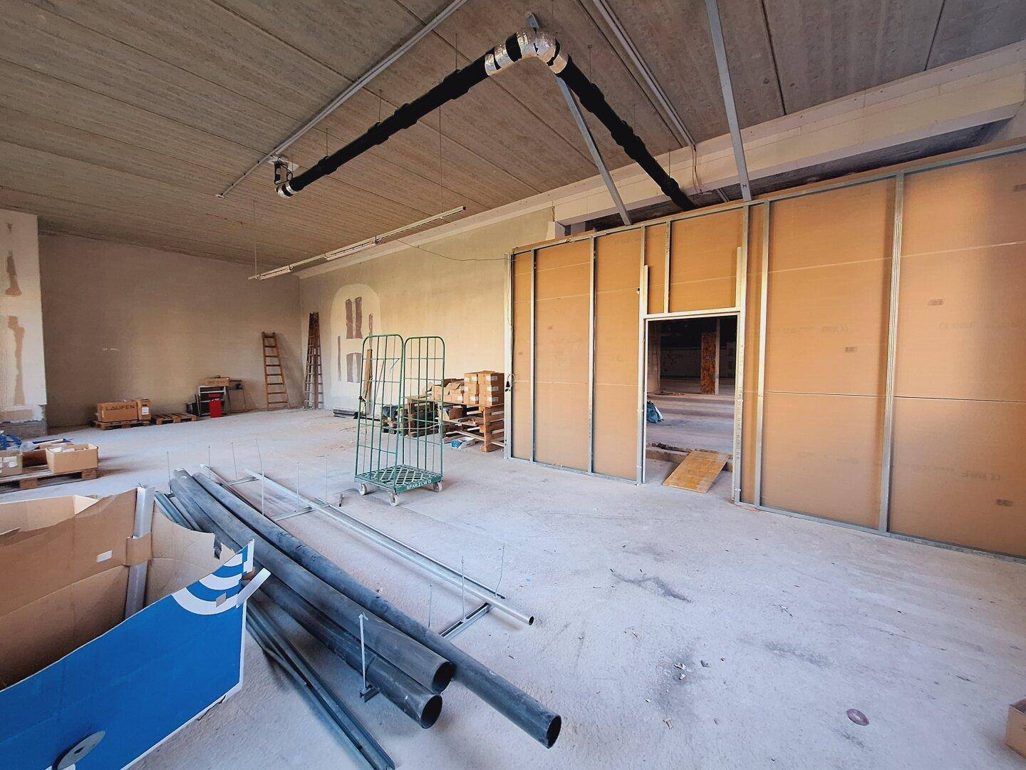 Gewerberaum im Rohbau mit sichtbaren Rohren und Deckenkonstruktion, bereit für den Innenausbau.