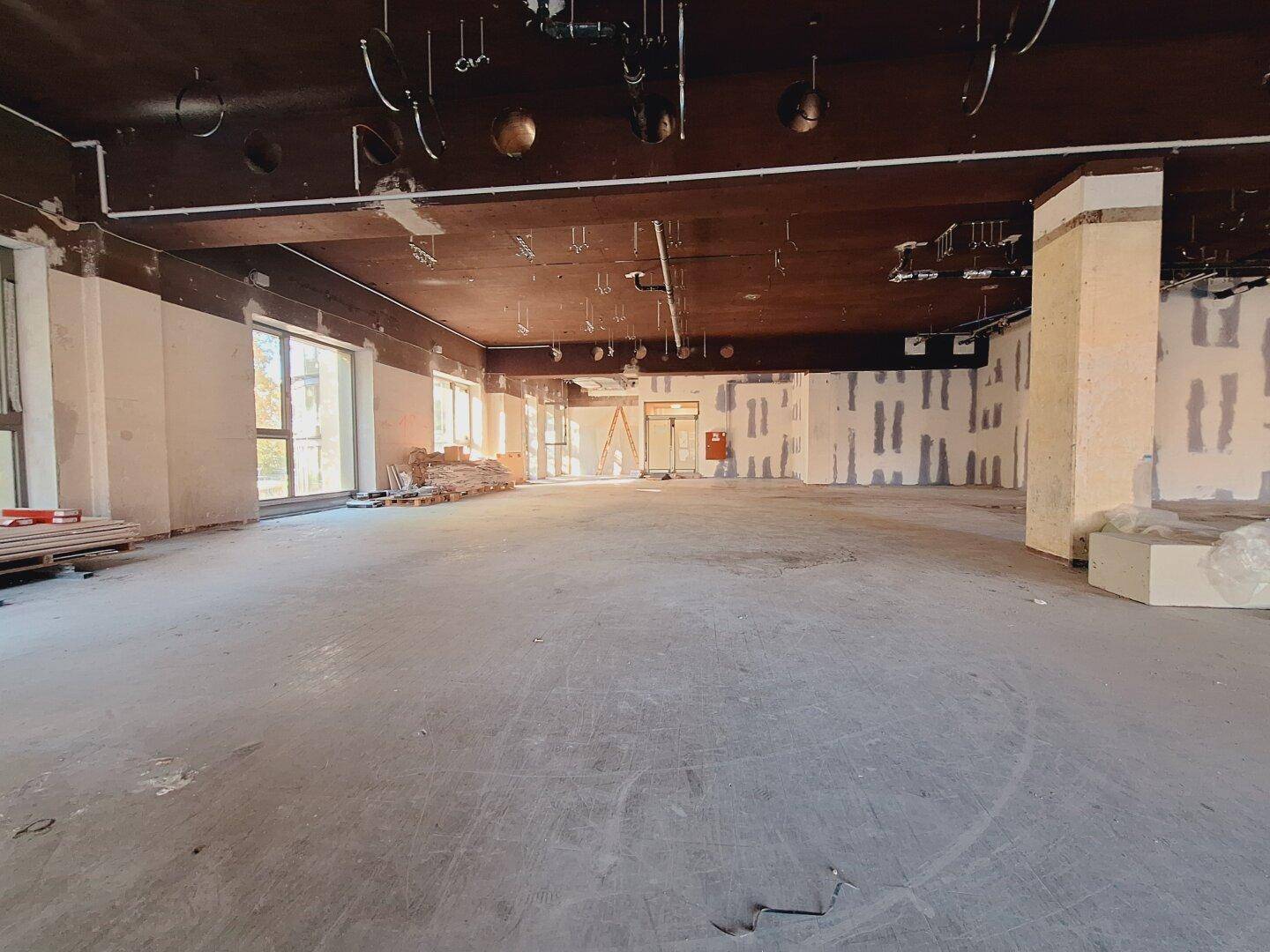 Weitläufiger Gewerberaum im Rohbau mit großen Fenstern und viel Tageslicht, bereit für den Ausbau.