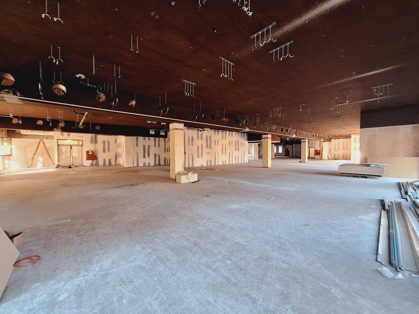 Weitläufiger Gewerberaum im Rohbau mit Säulen und sichtbaren Deckeninstallationen.