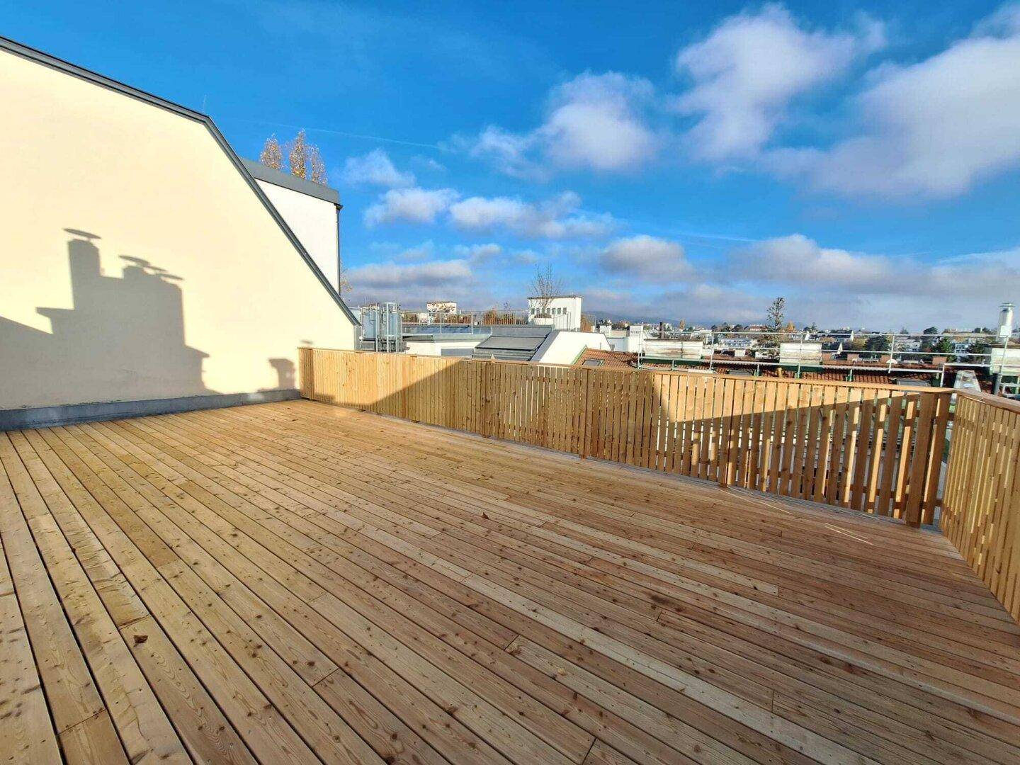 Große Dachterrasse mit neuem Holzbelag und Holzzaun unter blauem Himmel.