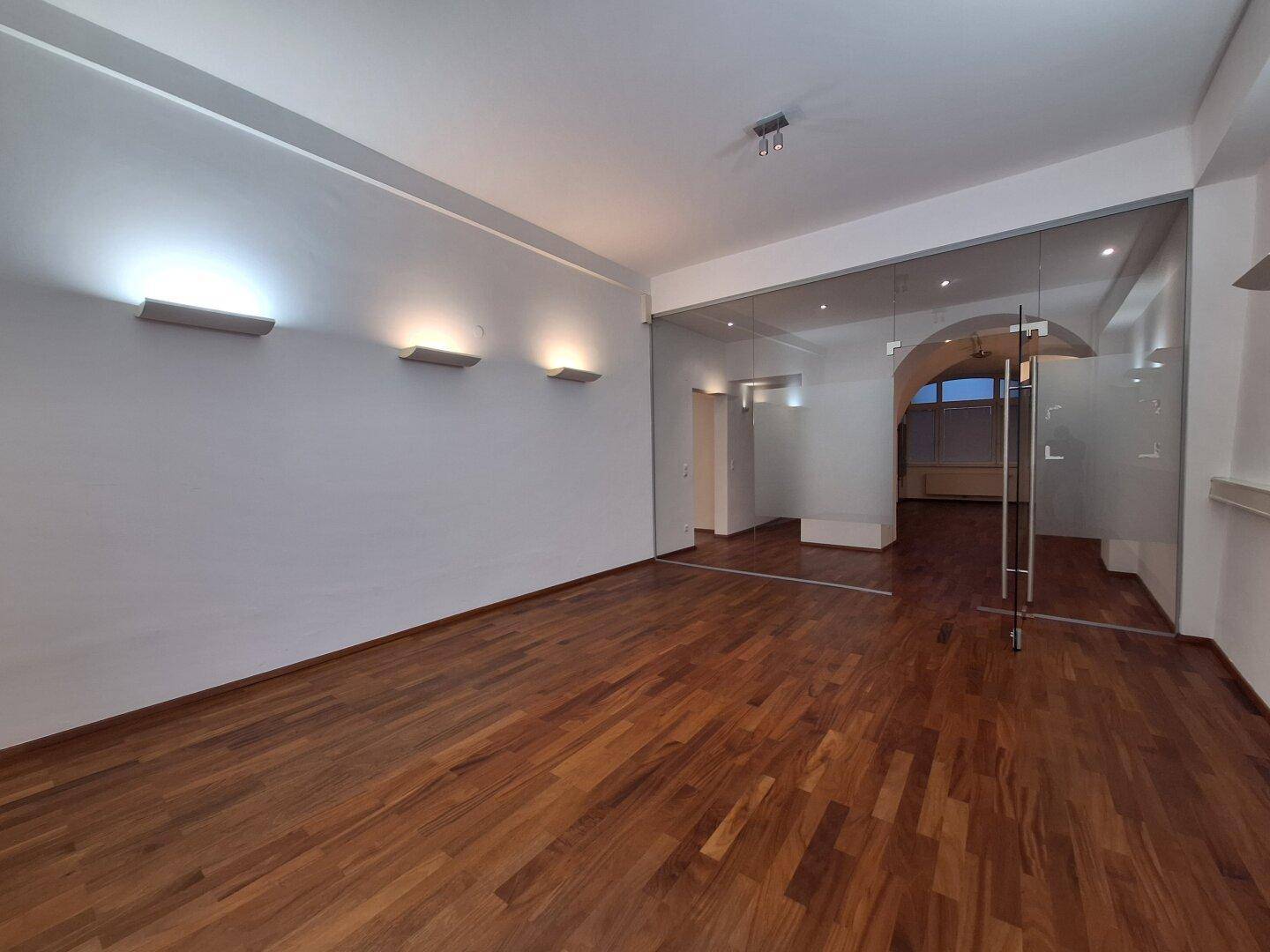 Heller Büroraum mit Holzboden und großen Fenstern, die für viel Tageslicht sorgen.