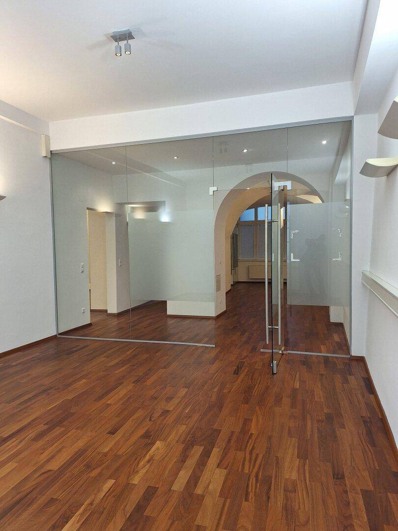 Heller Büroraum mit Holzboden und Glaswänden, die den Blick auf angrenzende Bereiche freigeben.