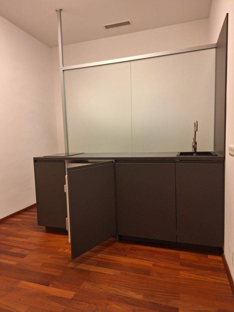 Moderne Küchenzeile mit dunklen Schränken und Spüle, ideal für eine kleine Büroküche.