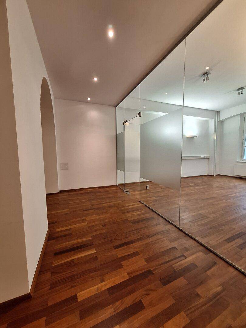 Heller Büroraum mit Holzboden und einer großen Spiegelfläche, die den Raum optisch erweitert.