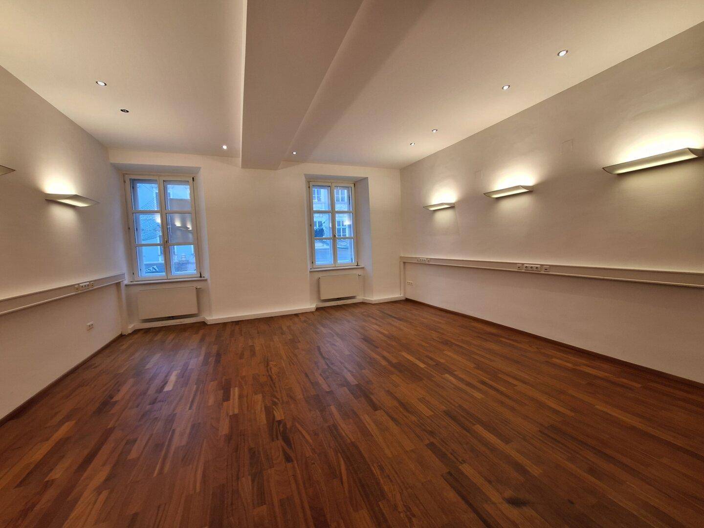 Heller Büroraum mit Holzboden und großen Fenstern, die für viel Tageslicht sorgen.
