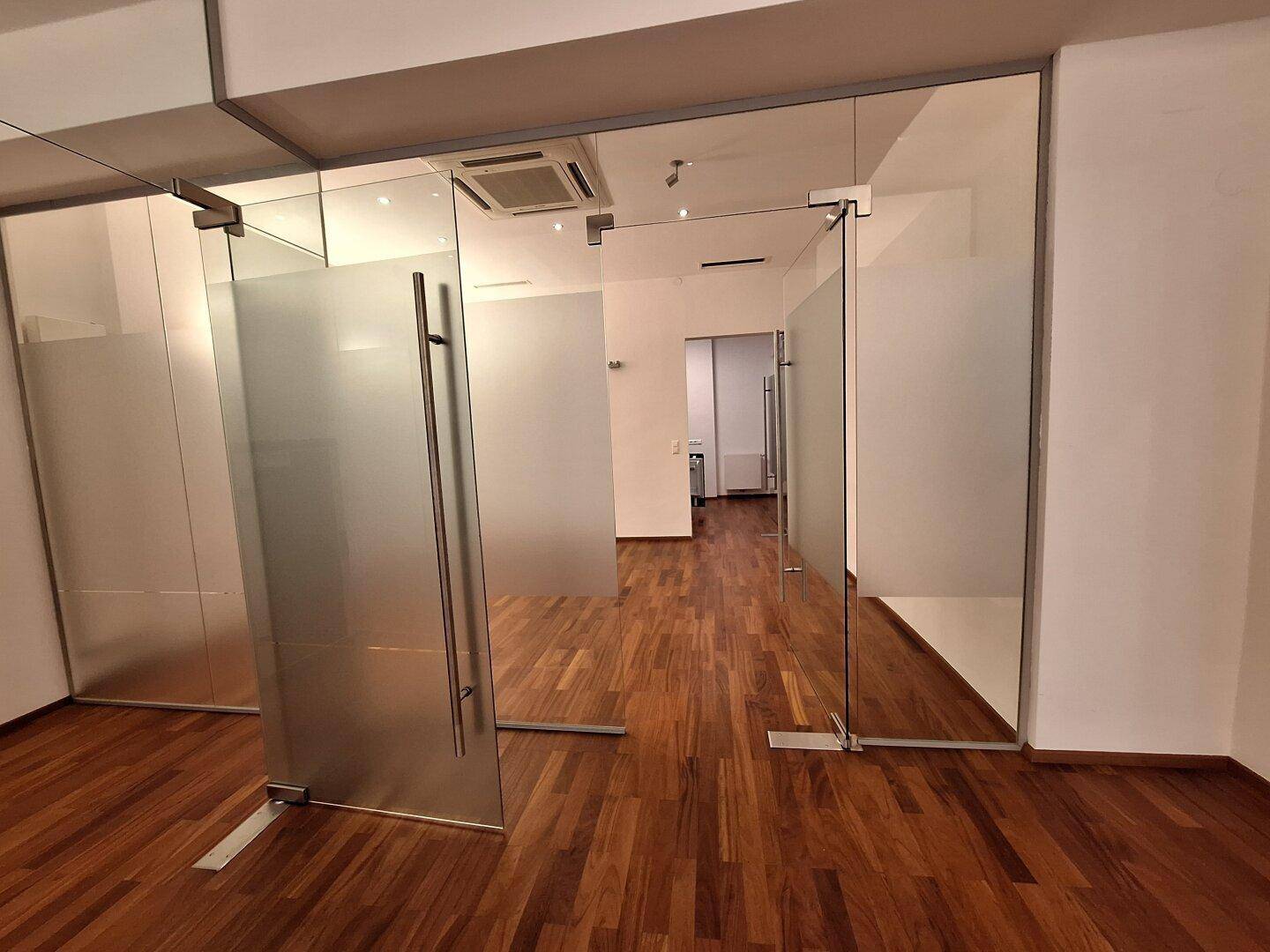 Moderner Büroraum mit Holzboden und Glaswänden, die für eine offene und helle Arbeitsumgebung sorgen.
