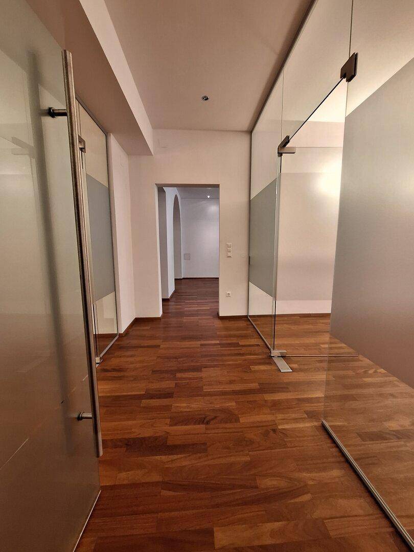 Moderner Flur mit Holzboden und Glaswänden, die Transparenz und eine offene Raumgestaltung fördern.
