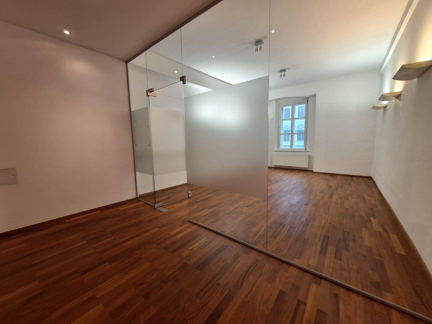 Heller Büroraum mit Holzboden und einer großen Spiegelfläche, die den Raum optisch erweitert.