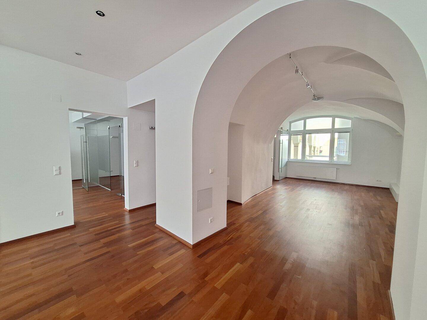 Großer Büroraum mit beeindruckenden Gewölbedecken und großen Fenstern, die viel Tageslicht hereinlassen.