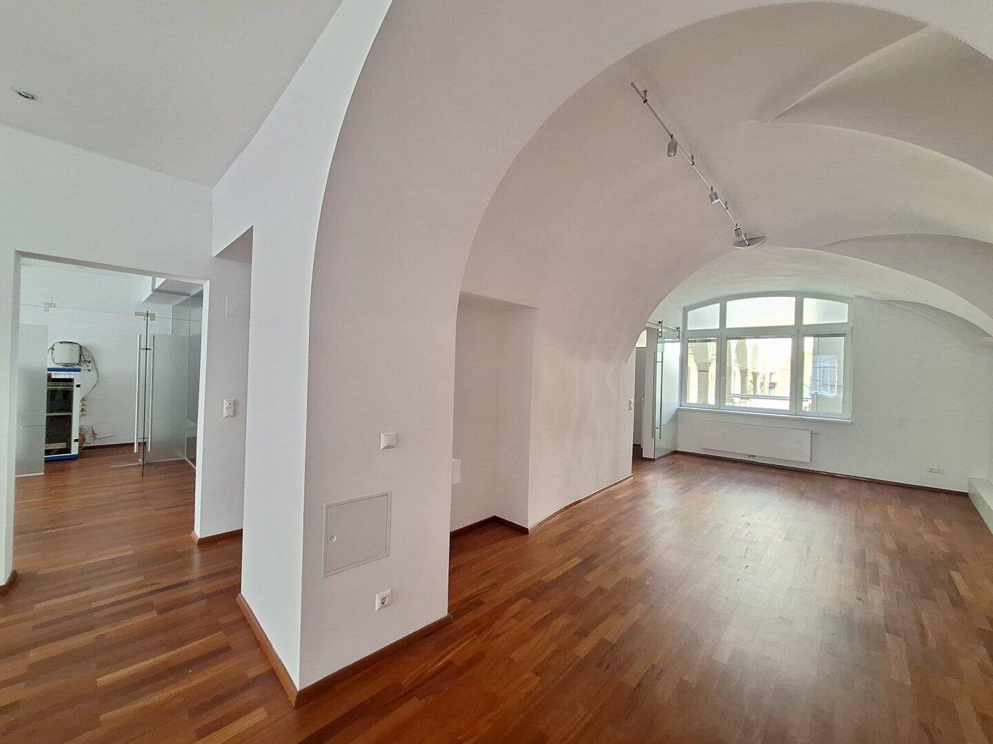 Großer Büroraum mit beeindruckenden Gewölbedecken und großen Fenstern, die viel Tageslicht hereinlassen.