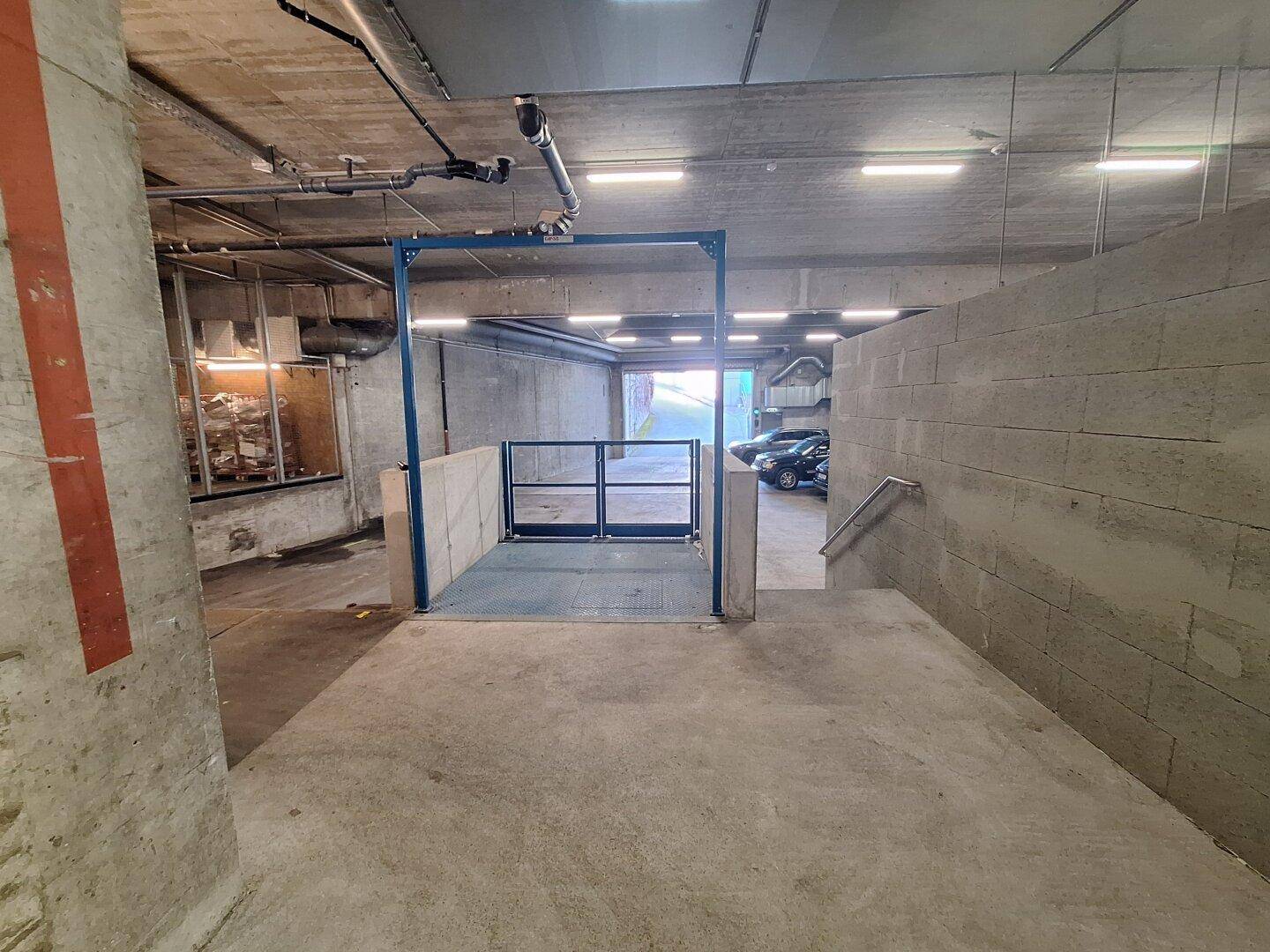 Tiefgaragenzufahrt mit Rampe und Schranke, die zu weiteren Parkplätzen führt.