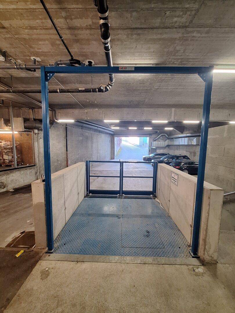 Tiefgaragenzufahrt mit blauer Metallkonstruktion und Schranke, die zu weiteren Parkplätzen führt.