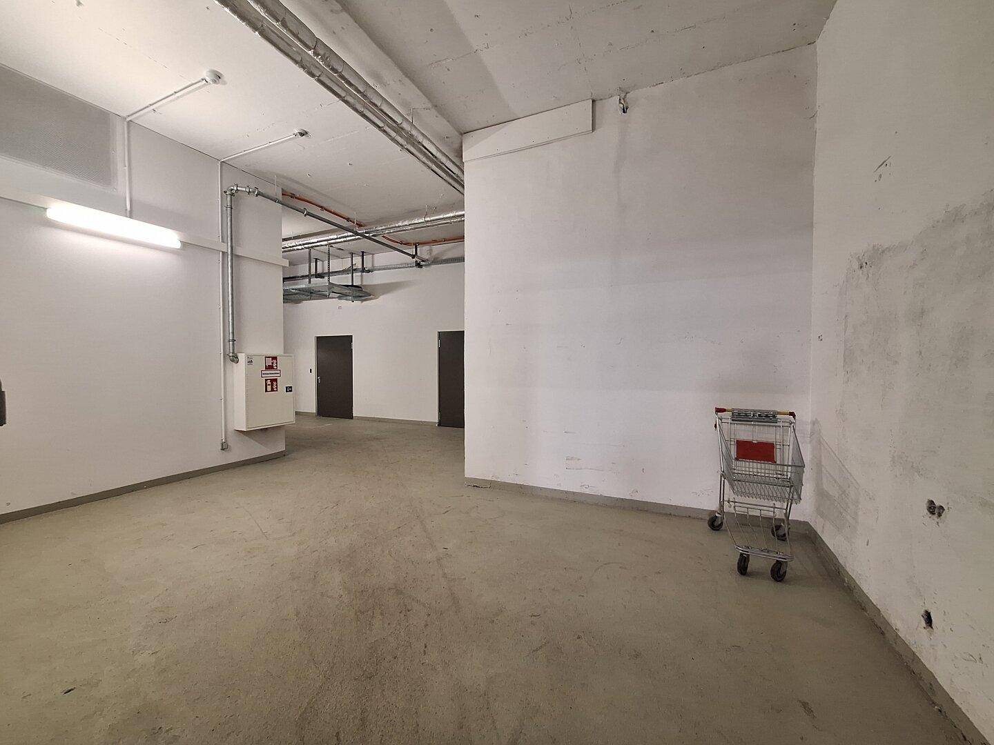 Lagerraum mit weißen Wänden, Betonboden und einem Einkaufswagen, bereit zur Nutzung.