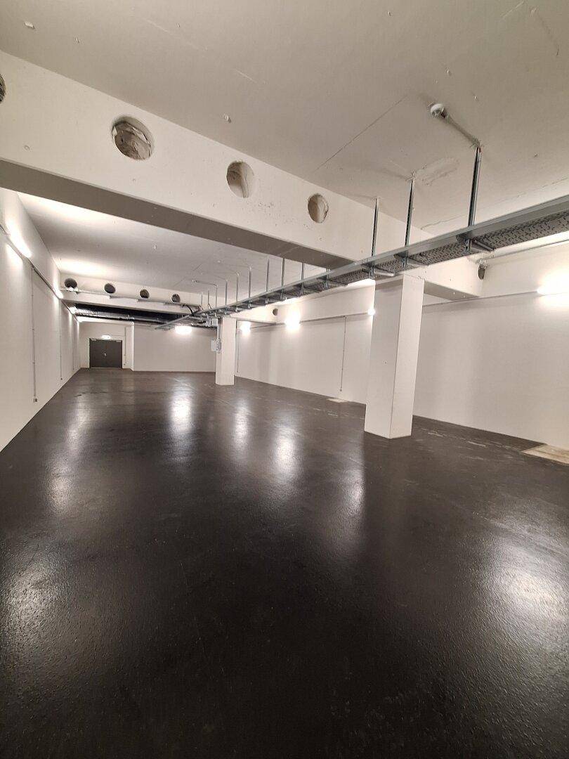 Großer Lagerraum mit hohen Decken, Säulen und sichtbaren Kabeltrassen, bereit zur Nutzung.