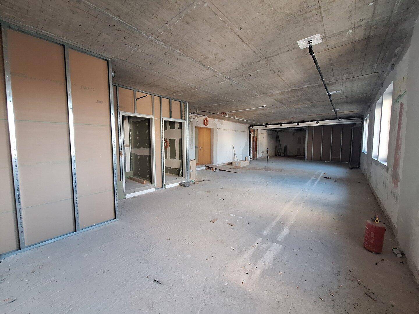 Geräumiger, unfertiger Büroraum mit Betonboden und -decke, ideal für individuelle Gestaltung.