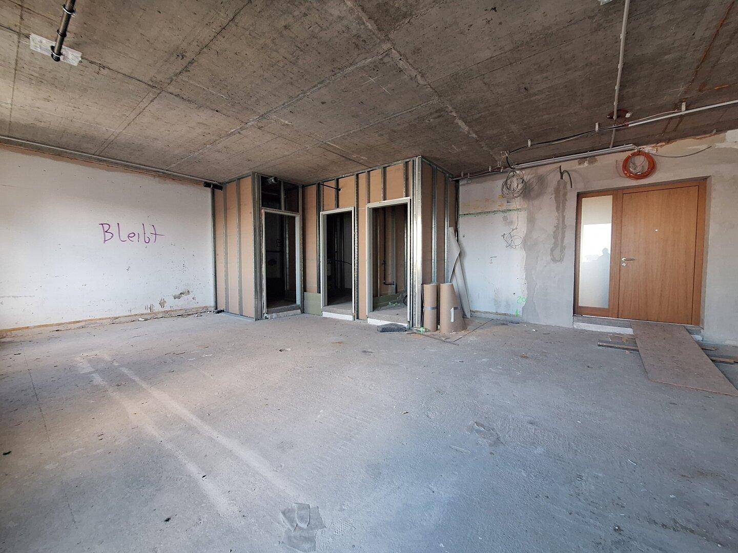 Großer, unfertiger Büroraum mit Betonboden und -decke, bereit für den Innenausbau.