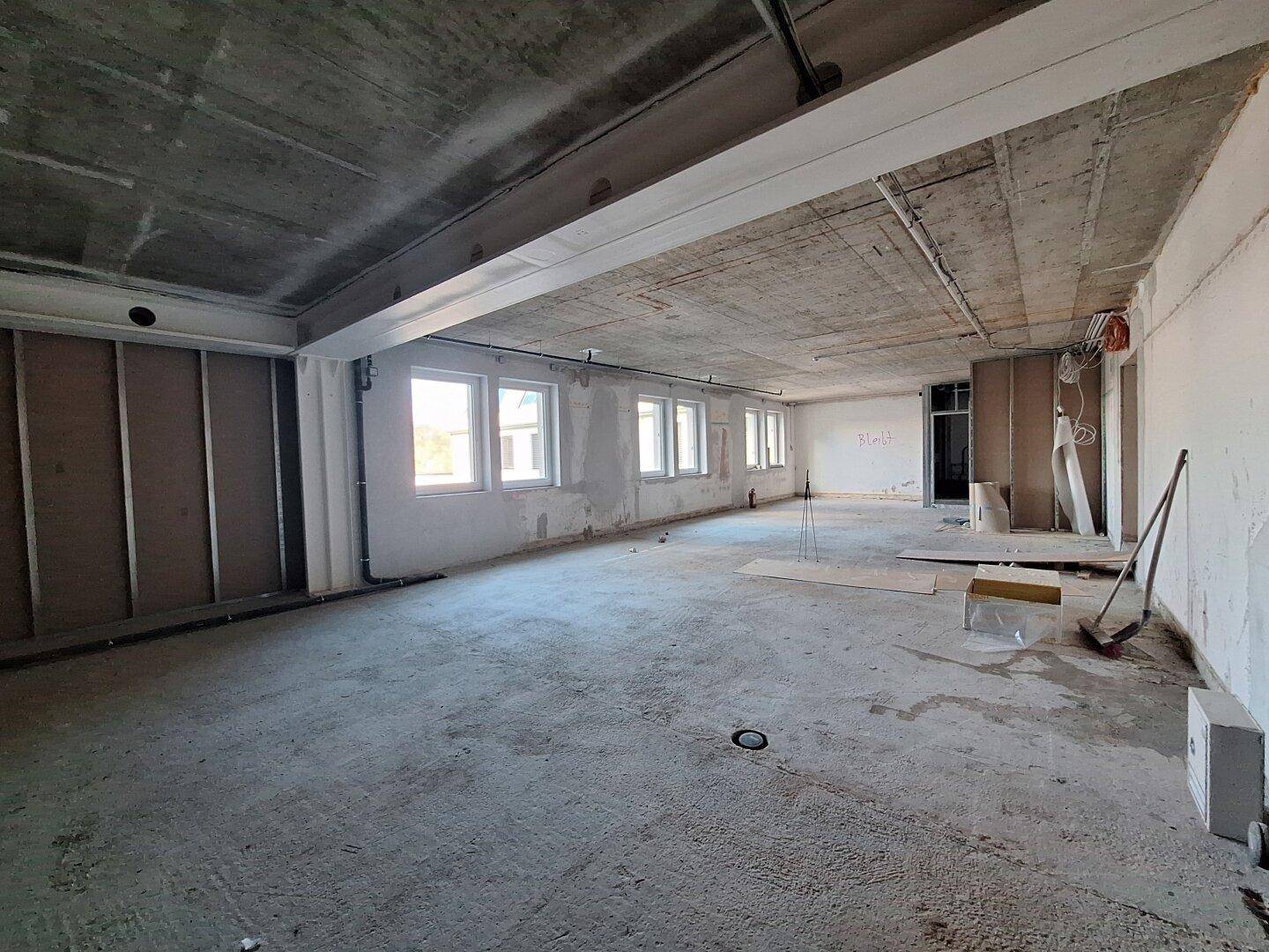 Großer, unfertiger Büroraum mit Betonboden und vielen Fenstern, bereit für den Innenausbau.