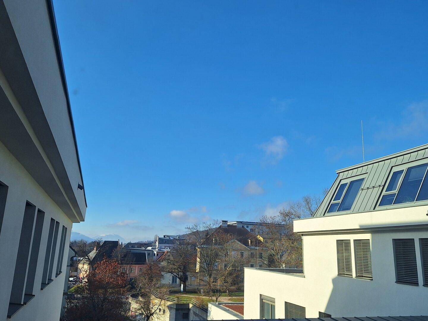 Weitblick zwischen modernen Gebäuden auf die umliegende Landschaft unter klarem blauem Himmel.