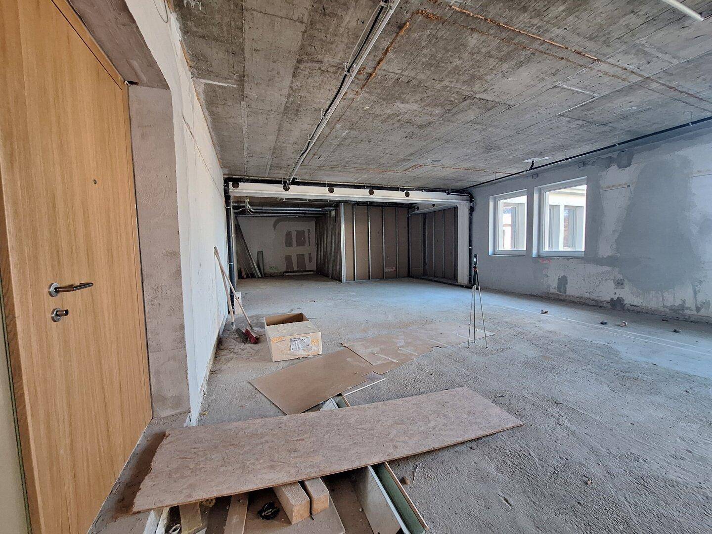 Großer, unfertiger Büroraum mit Betonboden und -decke, bereit für den Innenausbau.