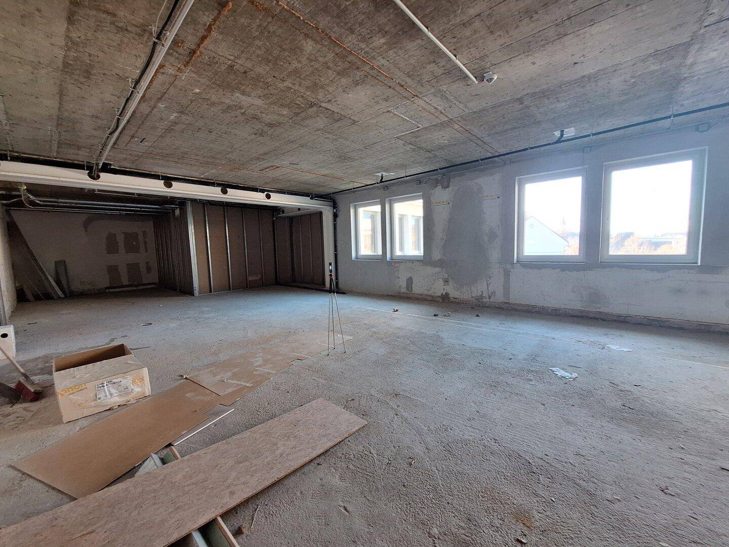 Großer, unfertiger Büroraum mit Betonboden und -decke, bereit für den Innenausbau.