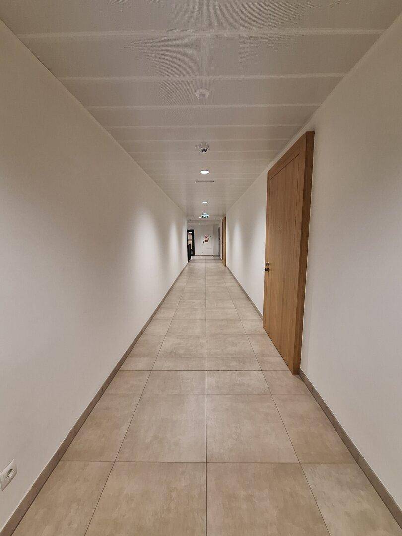 Sehr langer, heller Flur mit beigen Fliesen und Holztüren, der sich in die Ferne erstreckt.
