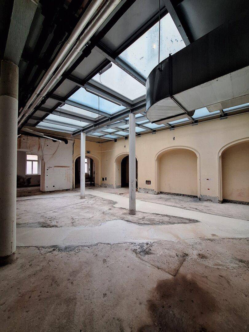 Heller, offener Innenraum mit einer beeindruckenden Glasdachkonstruktion und sichtbaren Säulen, ideal für gewerbliche Nutzung.