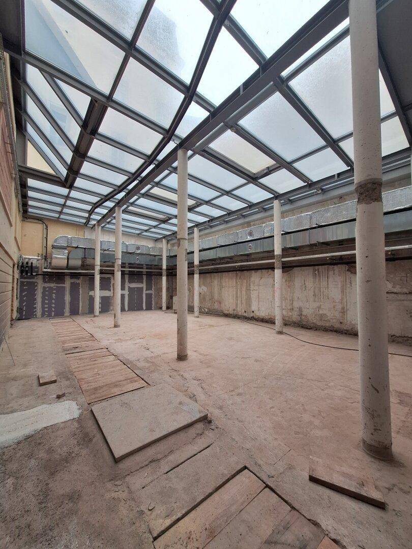Heller, offener Innenraum mit einer beeindruckenden Glasdachkonstruktion und sichtbaren Säulen, ideal für gewerbliche Nutzung.