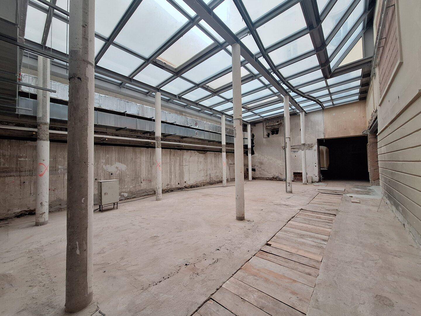 Heller, offener Innenraum mit einer beeindruckenden Glasdachkonstruktion und sichtbaren Säulen, ideal für gewerbliche Nutzung.