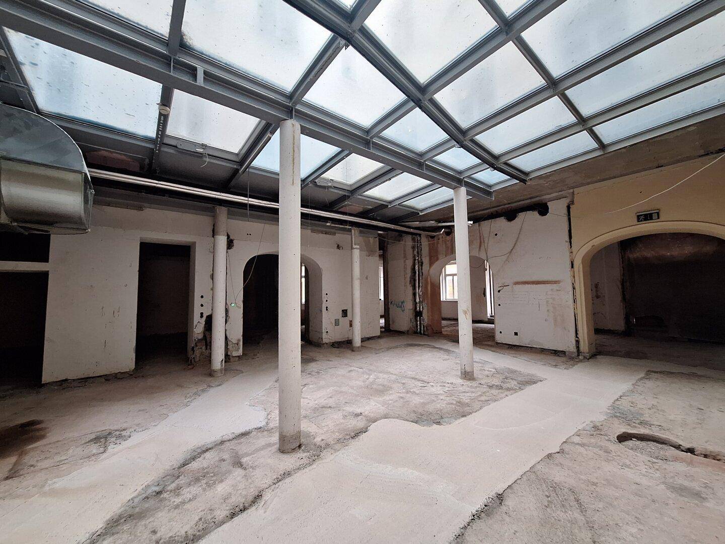 Heller, offener Innenraum mit einer beeindruckenden Glasdachkonstruktion und sichtbaren Säulen, ideal für gewerbliche Nutzung.