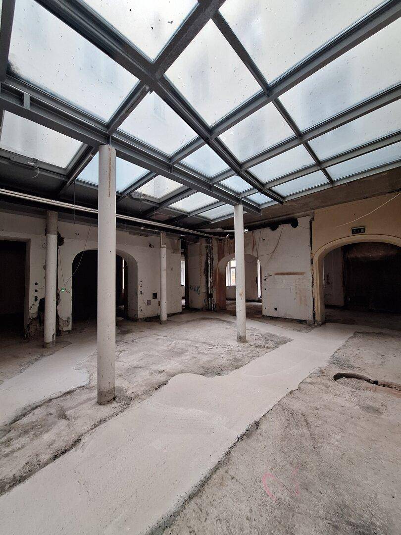 Geräumiger Innenraum mit einem modernen Glasdach und tragenden Säulen, der viel natürliches Licht hereinlässt.