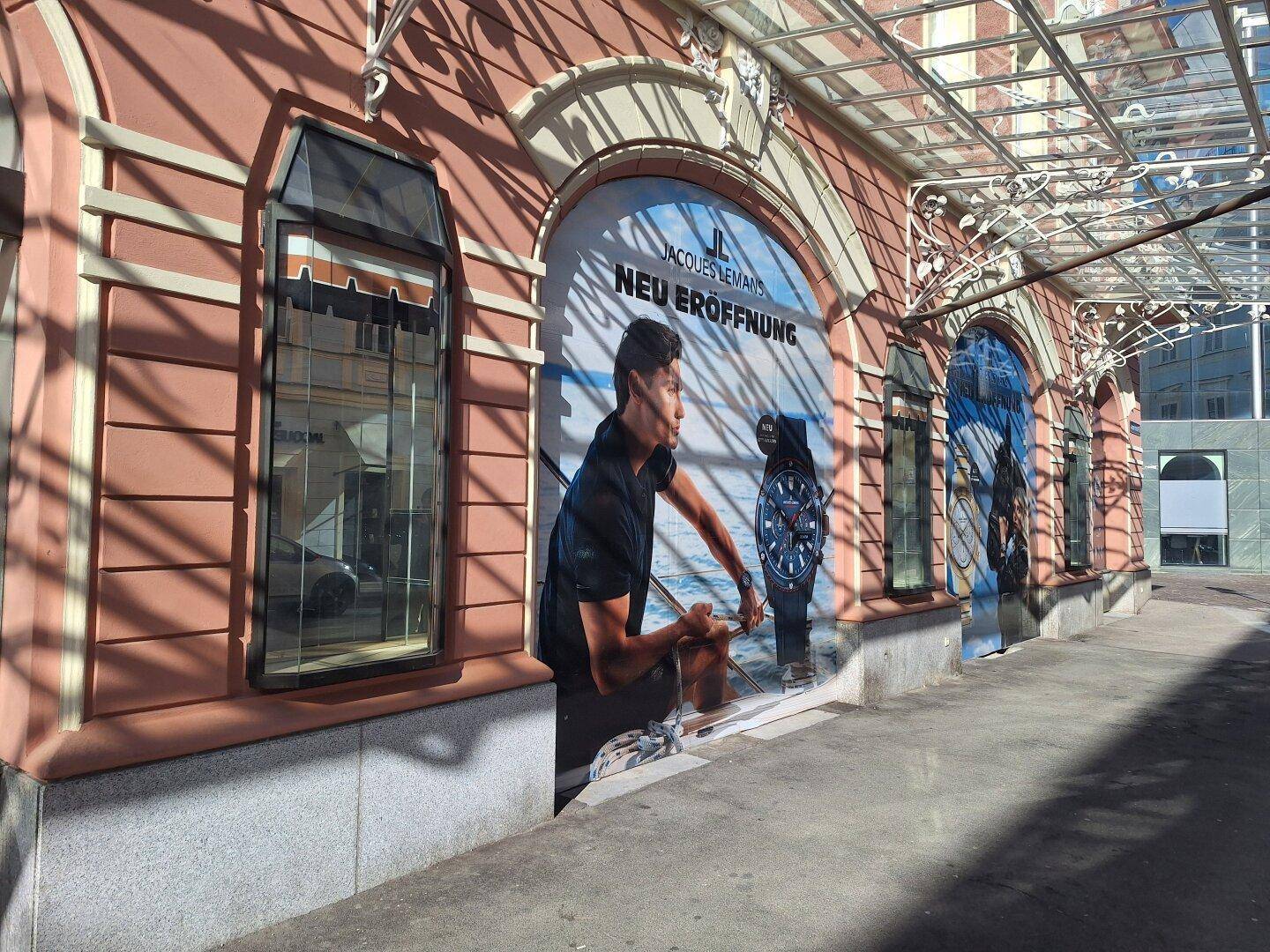 Fassade eines historischen Gebäudes mit großen Werbebannern für eine Neueröffnung und einem modernen Glasvordach.