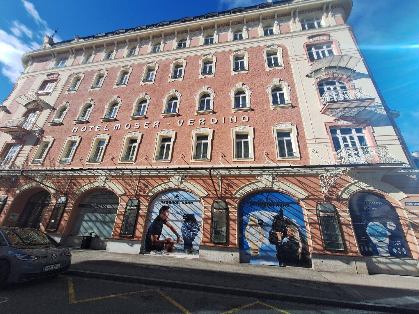 Gesamtansicht eines historischen Hotelgebäudes mit vielen Fenstern, Balkonen und Werbebannern im Erdgeschoss.
