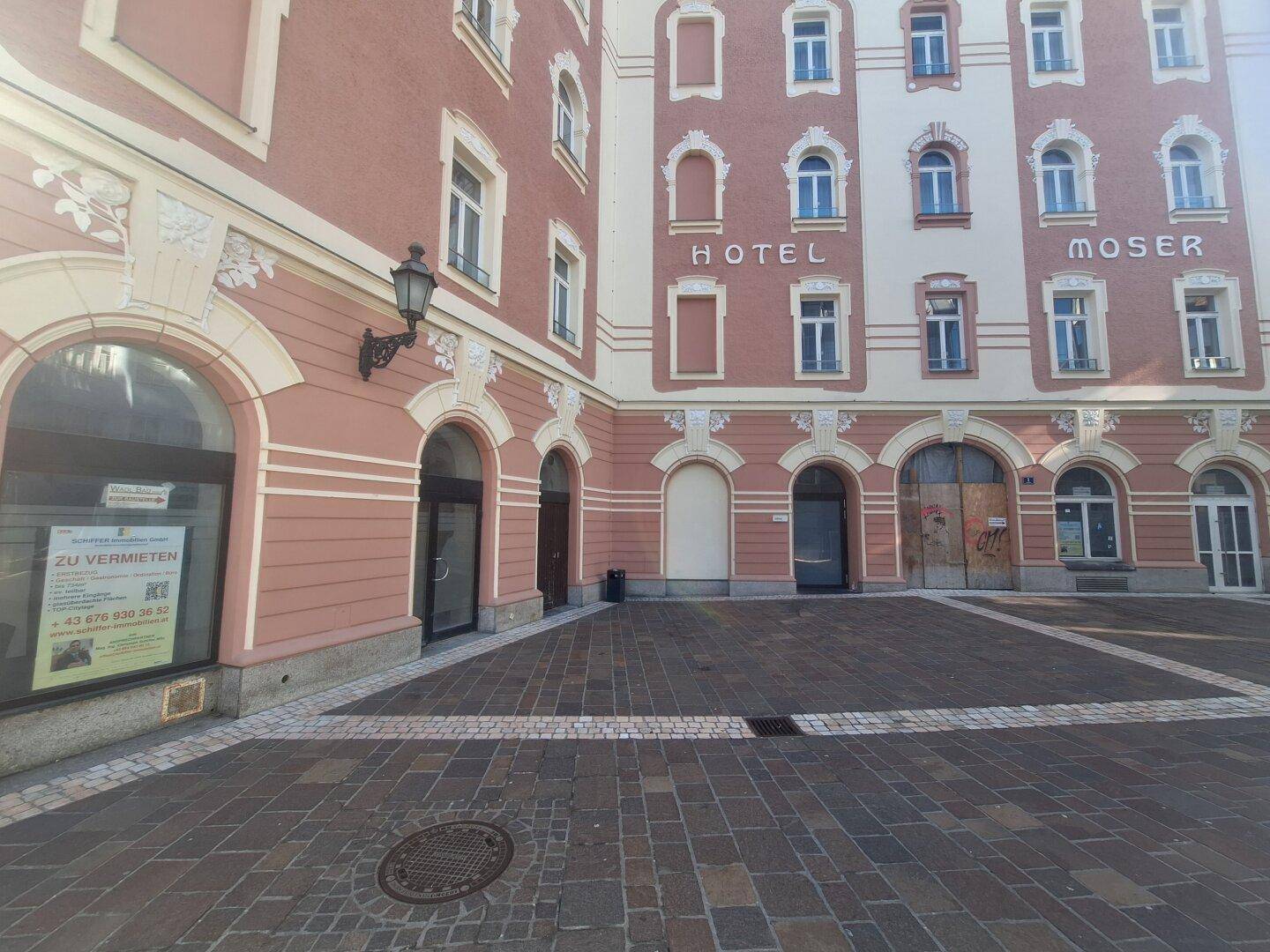 Innenhof eines Hotels mit gepflastertem Boden, einem 'Zu vermieten'-Schild und einer Wandlaterne.