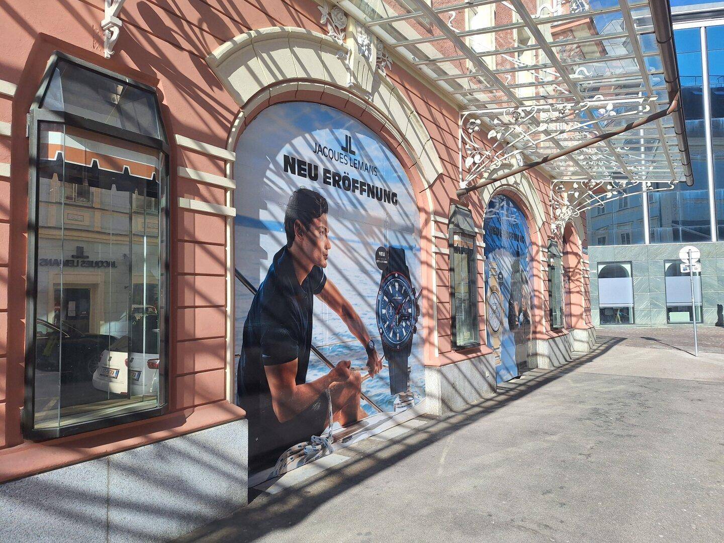 Fassade eines historischen Gebäudes mit großen Werbebannern für eine Neueröffnung und einem modernen Glasvordach.