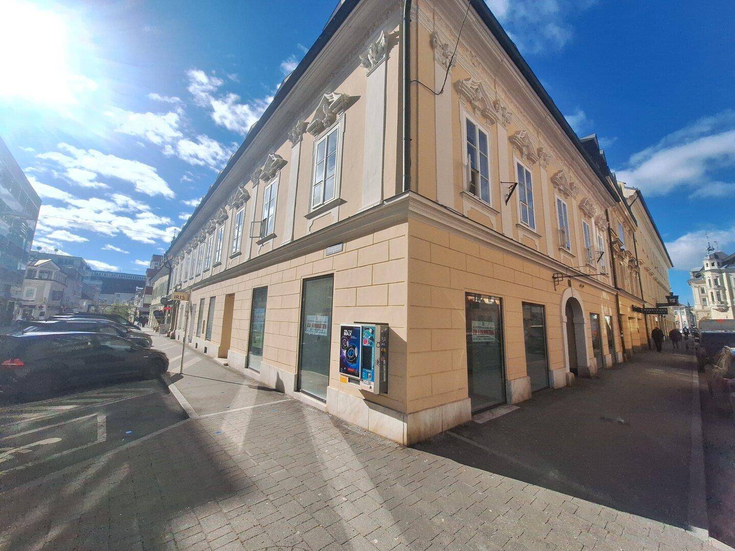 Historisches Gebäude mit Geschäften im Erdgeschoss und sonnigem Wetter, das die Fassade beleuchtet.