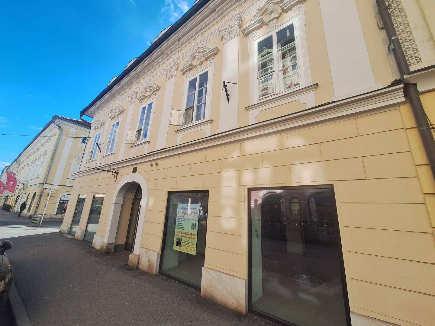 Historisches Gebäude mit Schaufenstern im Erdgeschoss und sonnigem Wetter, das die Architektur hervorhebt.