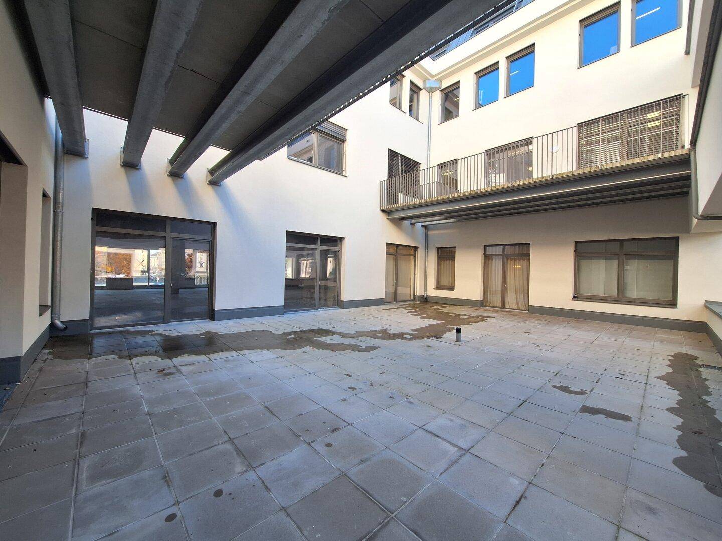 Helle, offene Terrasse mit robusten Bodenfliesen, integriert in eine moderne Gebäudestruktur mit mehreren Zugängen.