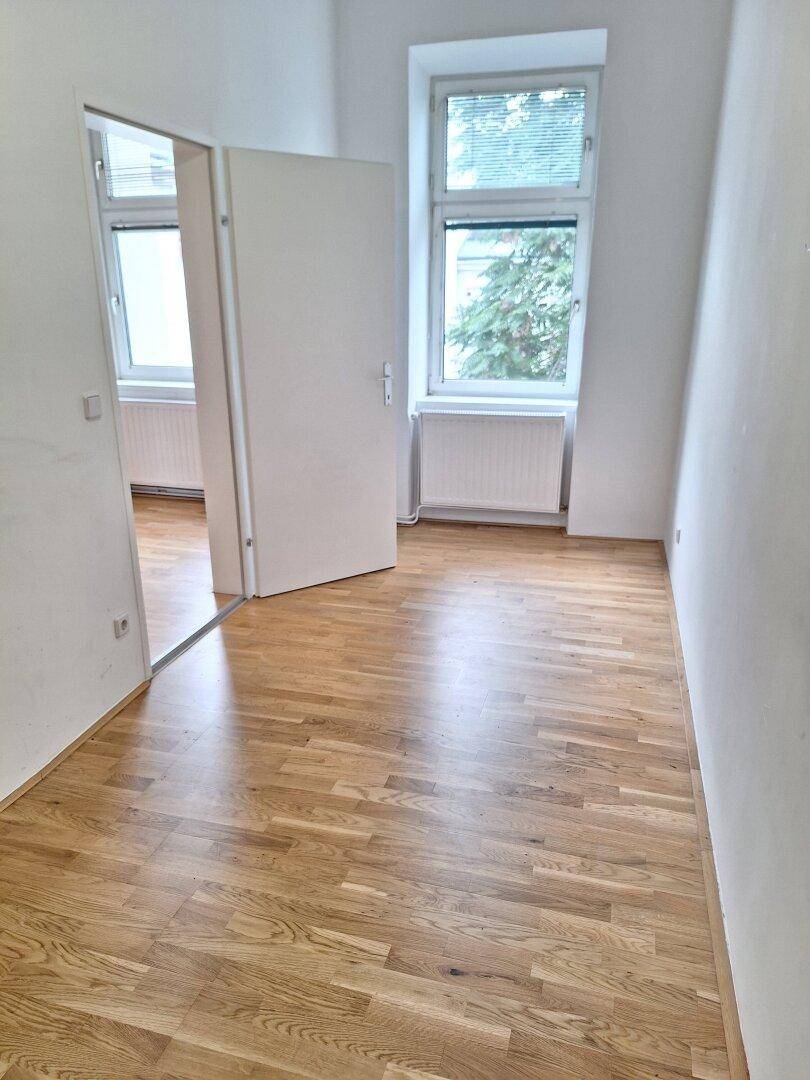 Helles Zimmer mit Parkettboden und Fenster mit Blick ins Grüne.