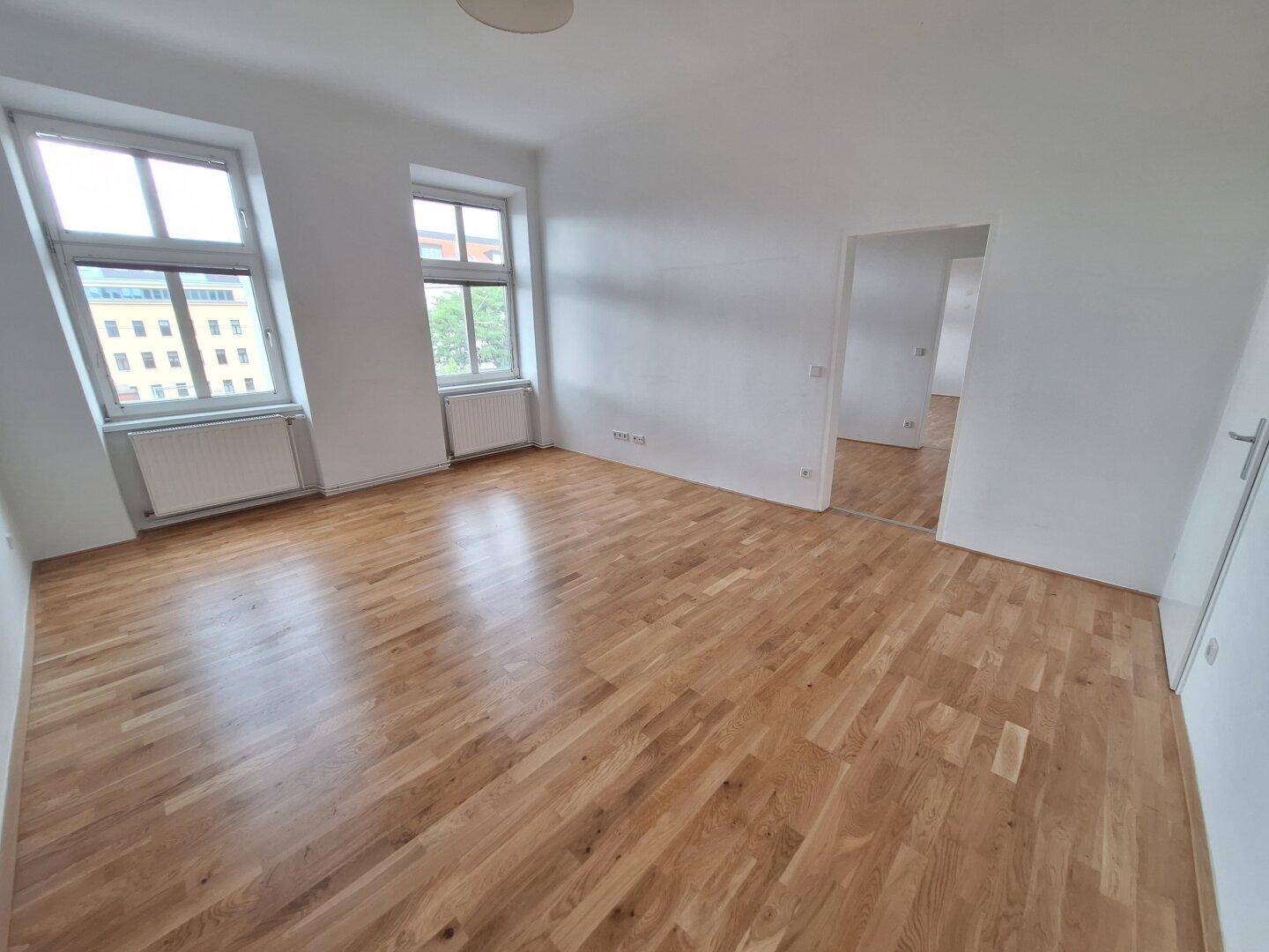 Geräumiges Wohnzimmer mit hellem Parkettboden und viel Tageslicht durch die Fenster.