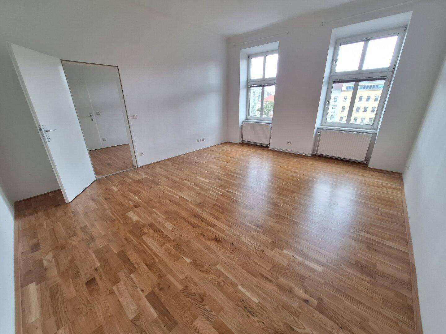 Heller Wohnbereich mit Laminatboden und Blick auf die umliegenden Gebäude.