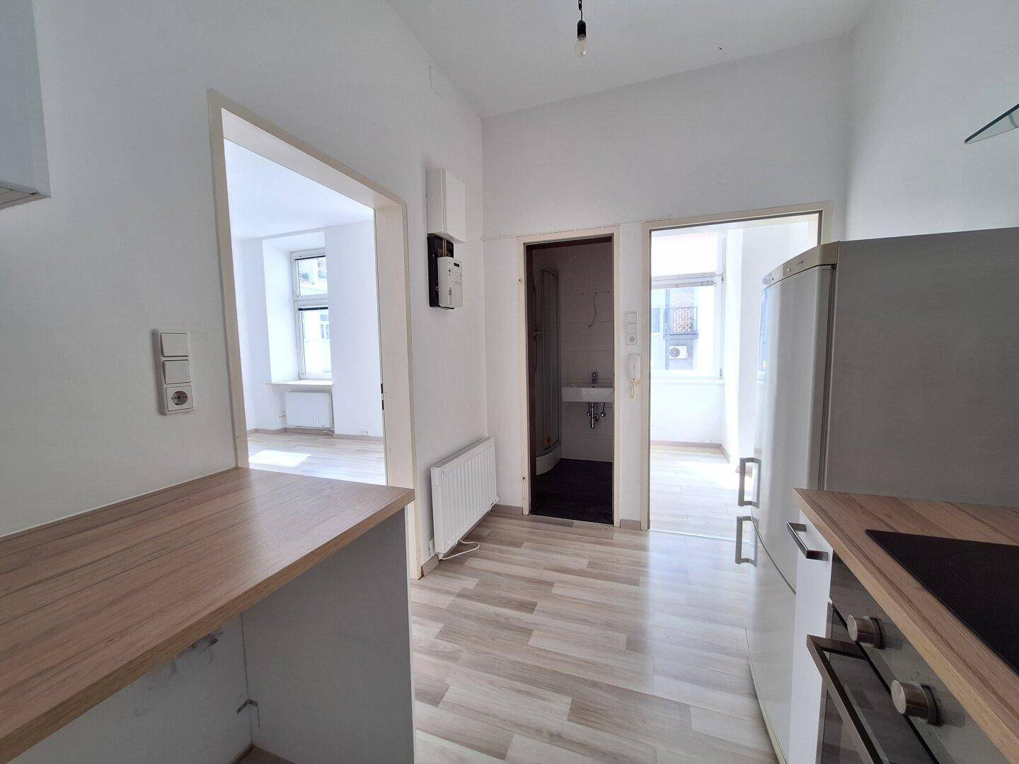 Küche mit hellem Laminatboden, Kühlschrank und Zugang zu weiteren Räumen.
