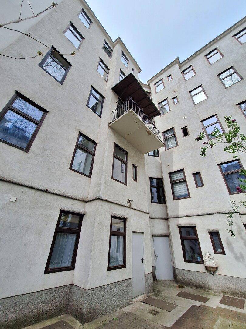 Blick auf den Innenhof eines Mehrfamilienhauses mit mehreren Fenstern und einem kleinen Balkon.
