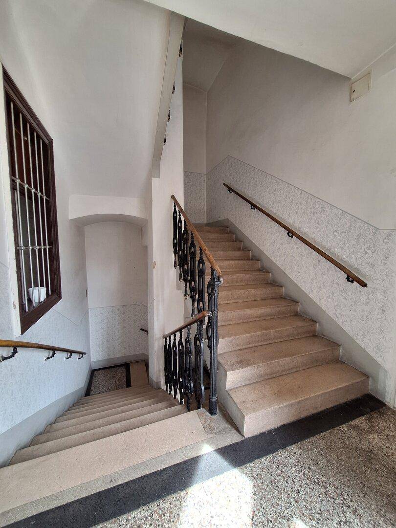 Treppenhaus eines Altbaus mit Steinstufen und schmiedeeisernem Geländer.