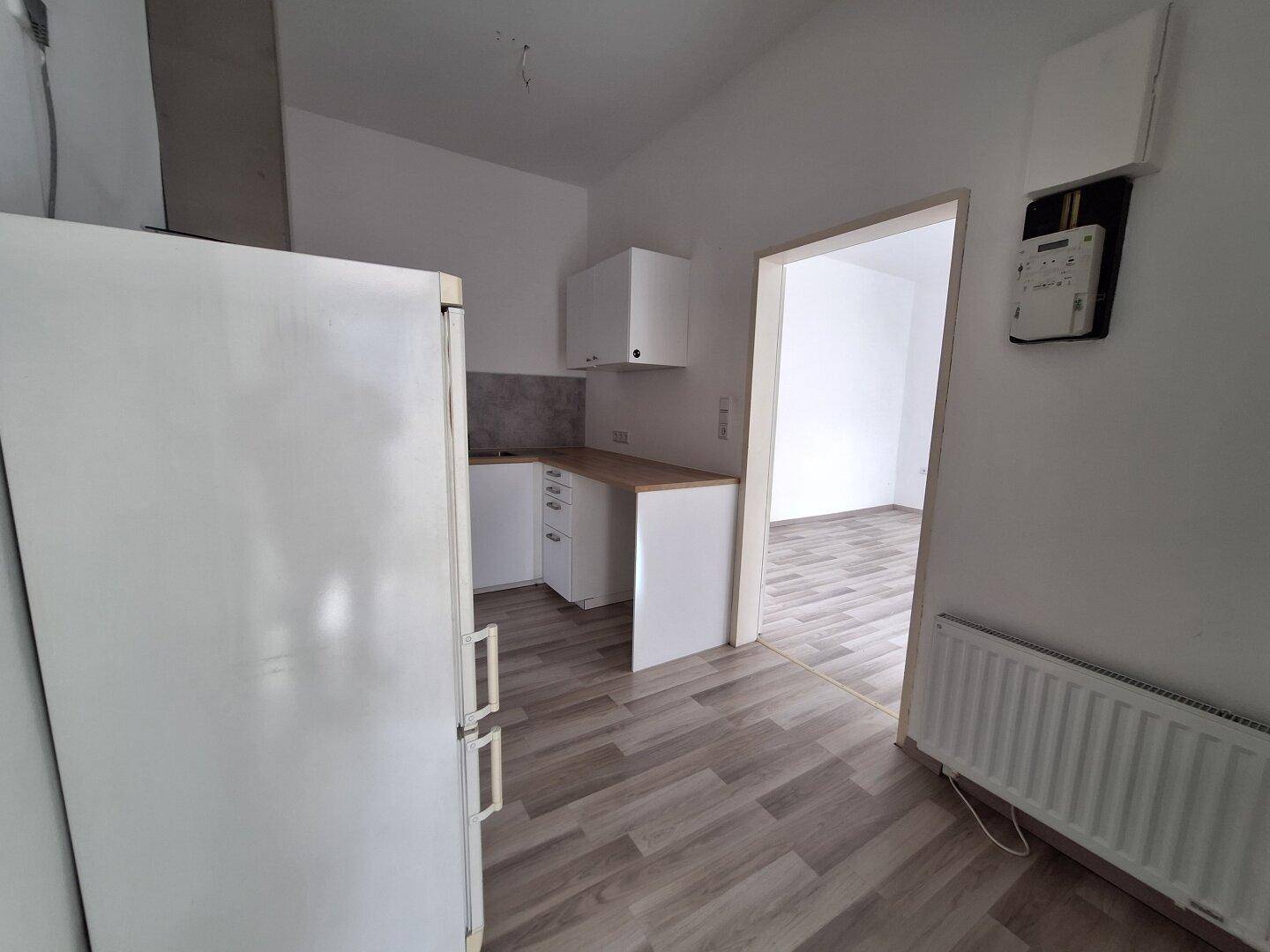 Kleine Küche mit weißem Kühlschrank und hellem Laminatboden.