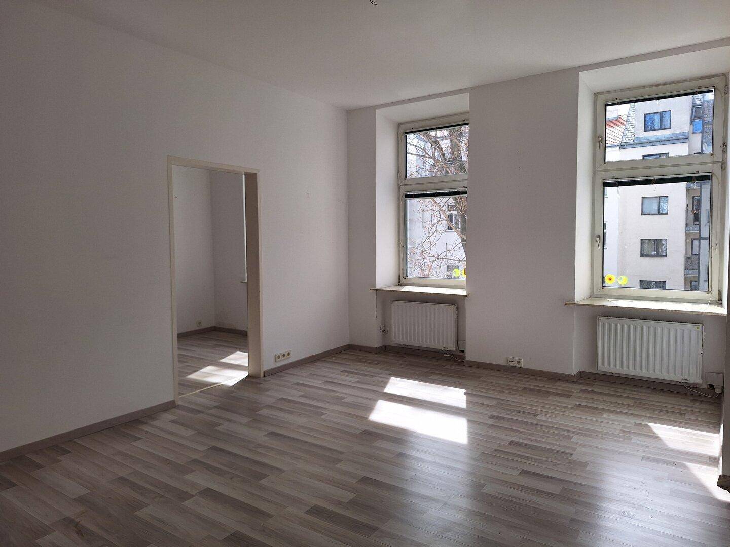 Heller Wohnbereich mit Laminatboden und Blick auf die umliegenden Gebäude.